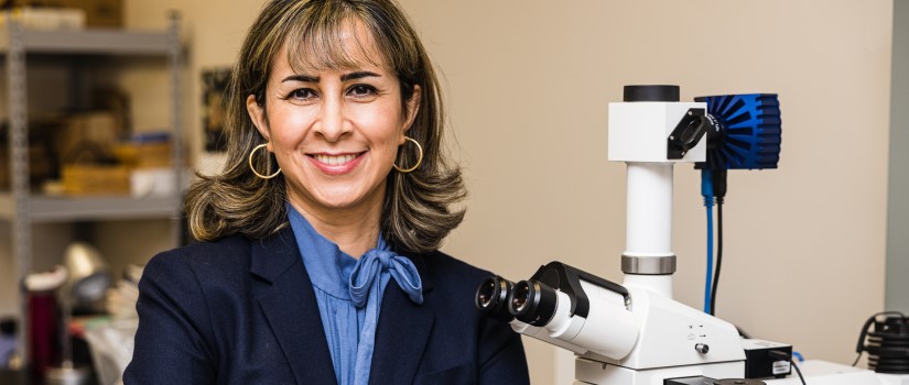 A portrait photo of Dr. Monirosadat “Sanaz” Sadati posing next to a high-powered microscope.