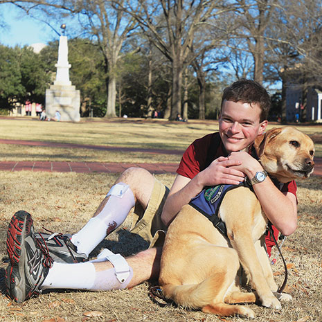 Jory Fleming hugs his service dog Daisy, a yellow lab, while seated on the Horseshoe. The Maxcy Monument is in the background.