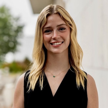 Headshot of a woman in a black shirt standing in front of a stone building.