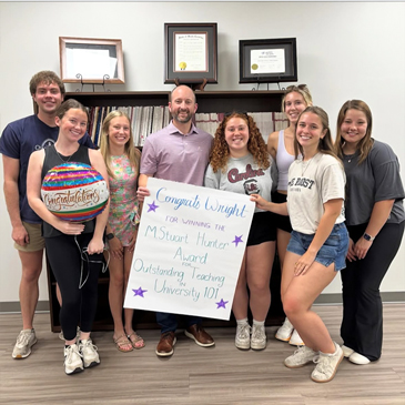 Wright Culpepper poses with a group of his 2025 students holding a congratulatory sign celebrating his M. Stuart Hunter Award for Outstanding Teaching in University 101.