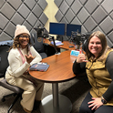 Photo of two women sitting in a podcast studio holding the spurs up hand signal