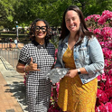 Shonta Sellers and Jessie McNevin stand in front of a pink flower bush beside the Thomas Cooper Library. There, they are holding a award for Garnet Bites in the shape of North and South Carolina.