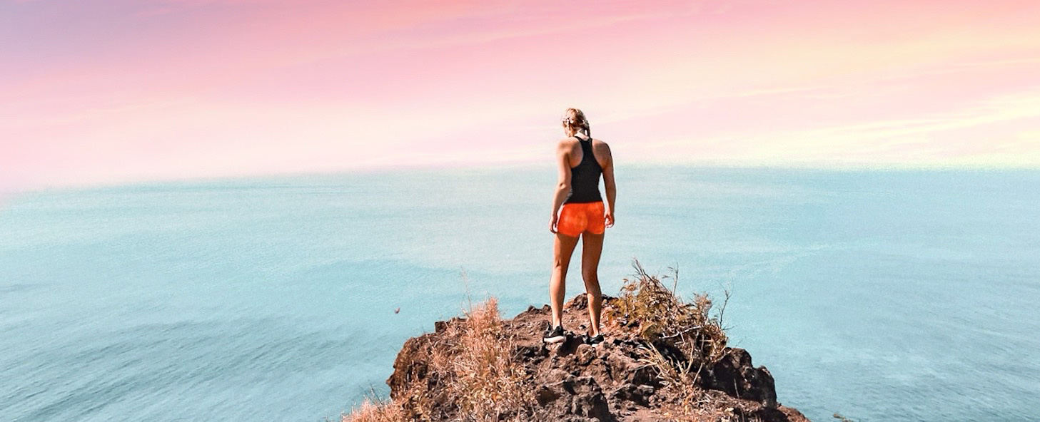 Girl standing on a cliff facing the sunset