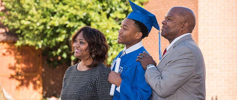 A male student in his graduation cap and gown posing for a photo with his parents.