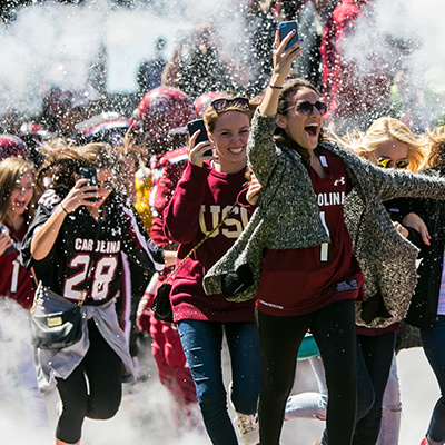 fans running through confetti and smoke at football game