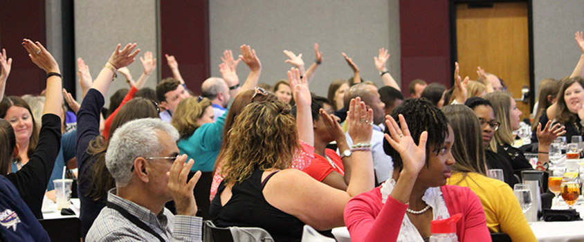 A conference room is full of people with their hands raised.