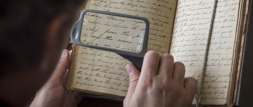 person reading a handwritten journal with a magnifying glass