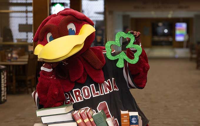 Cocky holding a shamrock on the main floor of the library