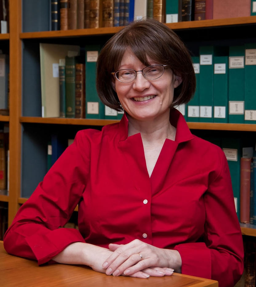 Elizabeth Sudduth sitting at a table in front a bookcase smiling
