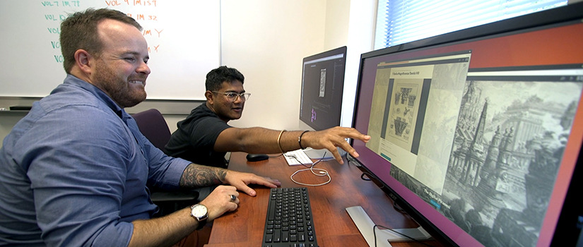 Instructor Jason Porter pictured with student Aniruth Sivakumar, who is pointing at one of multiple computer screens at a workstation