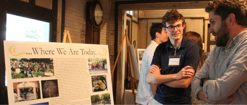 Student stands by poster and explains the content at the opening of the exhibit.
