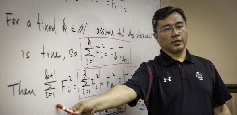 Dr. Bryan Lai next to whiteboard with math equations on it.