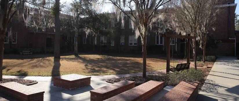 Brick benches and trees draped with Spanish moss outside a building on the USC Salkehatchie campus