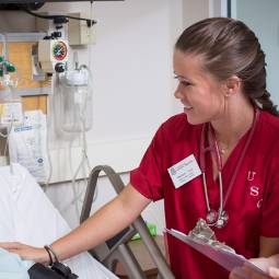 Female nursing student in red scrubs doing a bed check on a patient