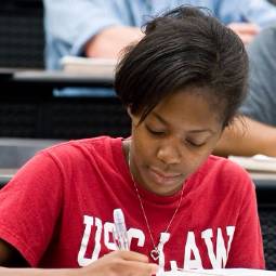 Close-up of student wearing read USC Law T-shirt and taking notes at a desk in a law classroom