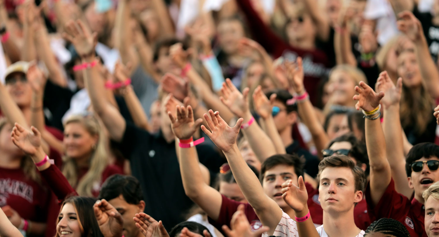 students raise their hands as part of the alma mater