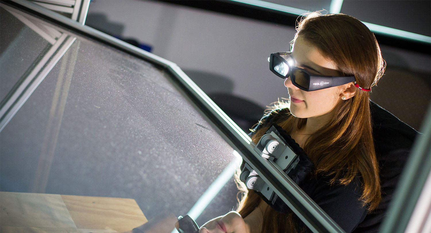 Student waring 3D goggles stares through a glass plane during an experiment. 