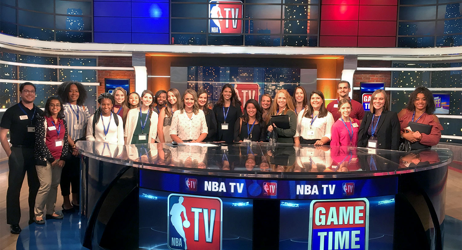 Group of students standing behind the news desk on the set of NBA TV Game Day.