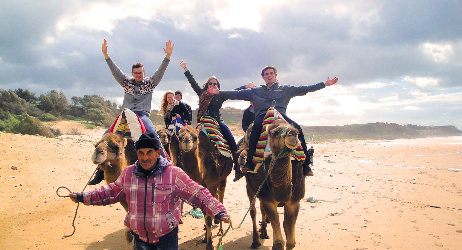 Group of students on camels with their arms raised. 