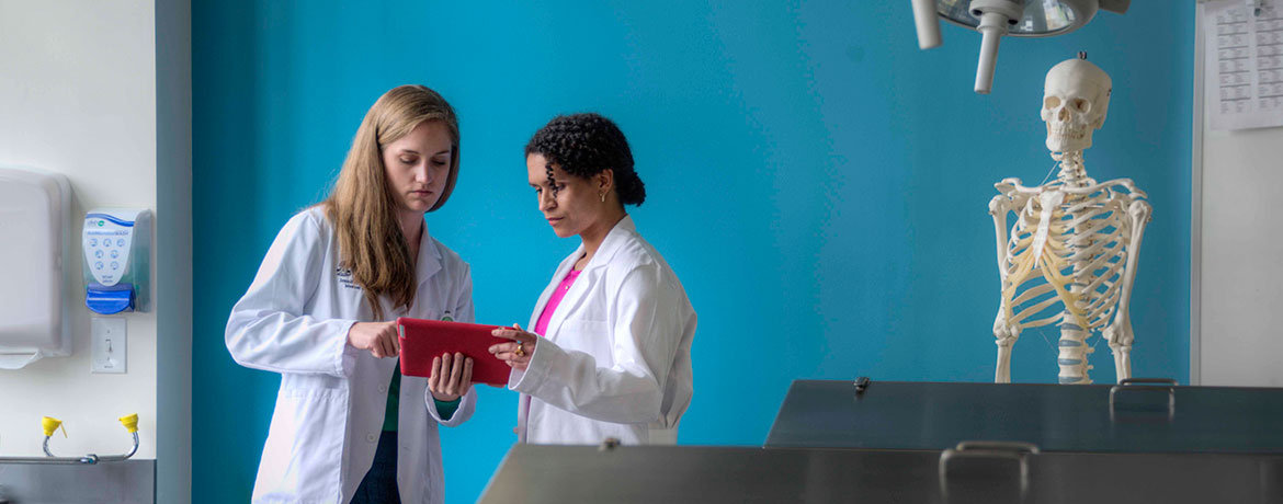 two students in lab coats studying a patient file in a lab