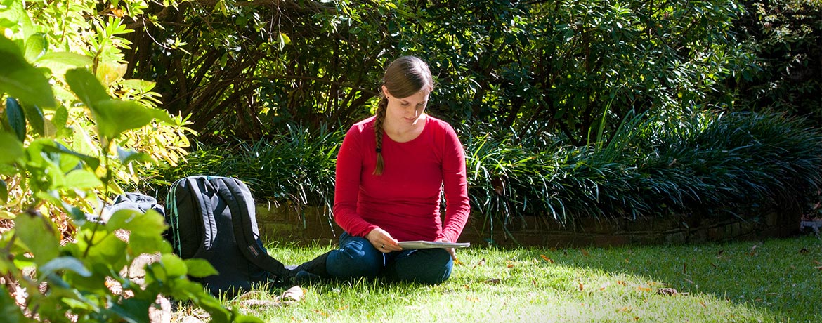student studying outdoors on campus surrounded by lush greenery