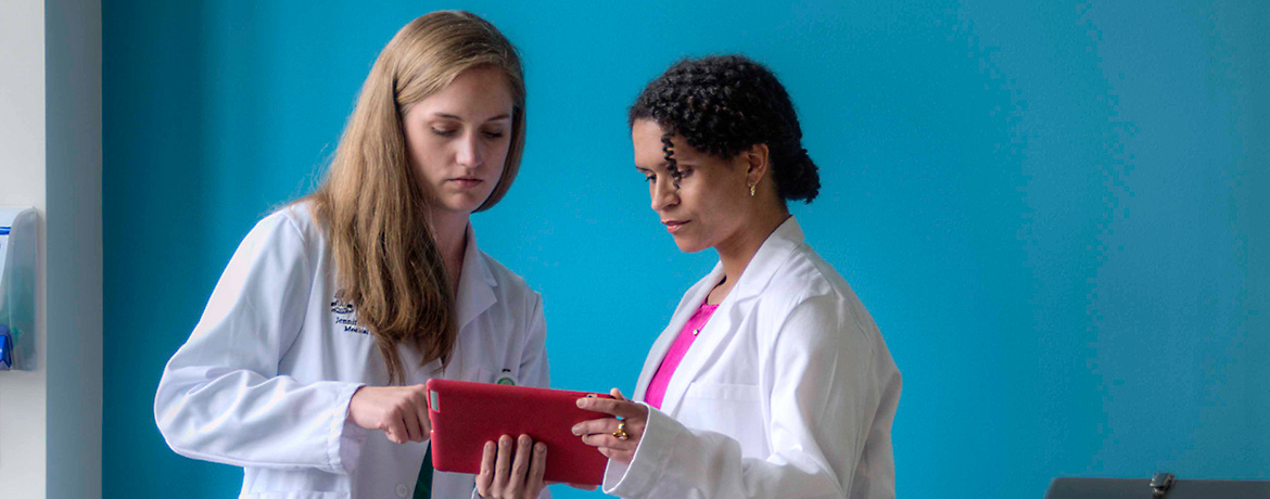 two students in lab coats consulting a tablet for information