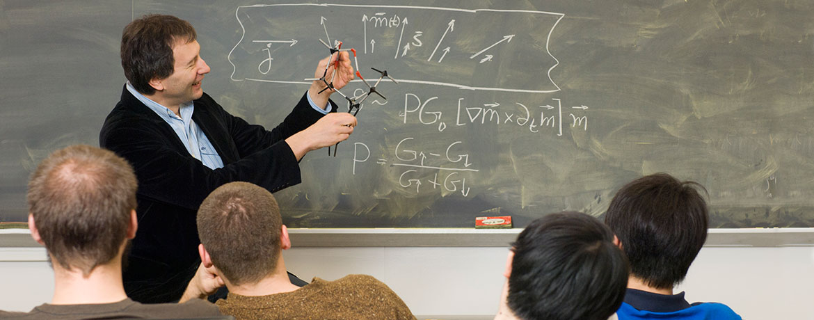 professor in front of a chalkboard explaining a theory to students