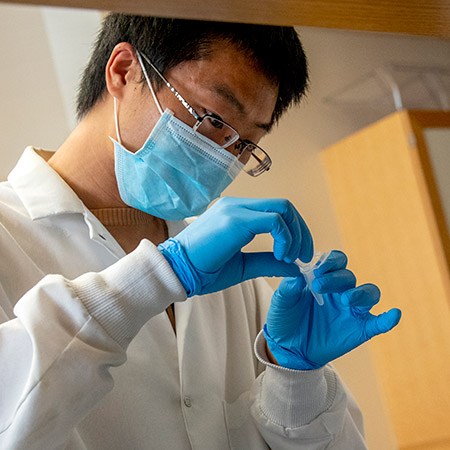 Researcher in a lab coat using a pipet in a lab. 