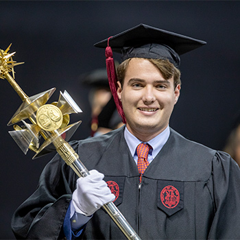 Student in regalia holding the university mase.