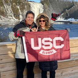 alumni travelers pose in front of a waterfall holding a USC flag