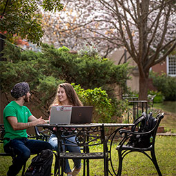 Two students sitting at an outdoor table talking with each other. 
