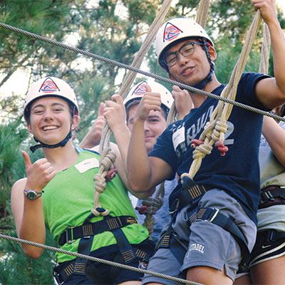 Students gathered together on the ropes course smiling and giving a thumbs up at the camera.