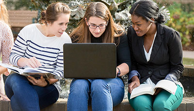 Three students sitting outside gathered around a laptop.