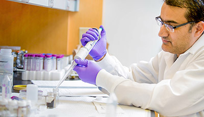 Researcher in a lab pipetting at a table.