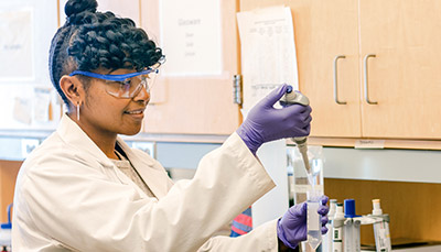 Student in a lab wearing lab safety gear using a pipette.