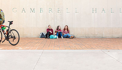 Three students talking, sitting outdoors at Gambrell Hall.