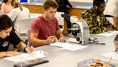 Students working in lab class at large tables with a microscope. 