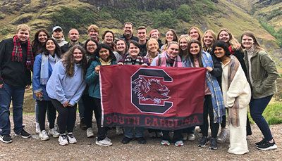 USC students holding a Gamecock flag with a mountain base in the background. 