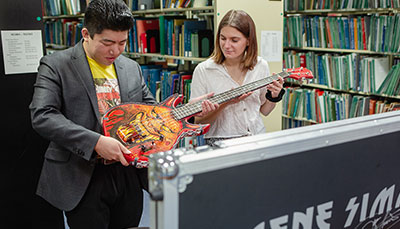 Two people inspecting a guitar in a library. 