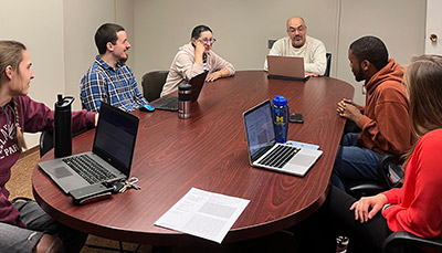 Students and faculty sitting around a table discussing.