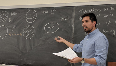 Faculty member pointing to mathematics writing on a chalkboard. 