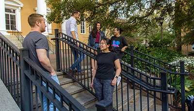 Five students talking to each other in front of a building on stairs.