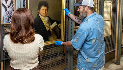 Two people taking a painting out of museum storage. 