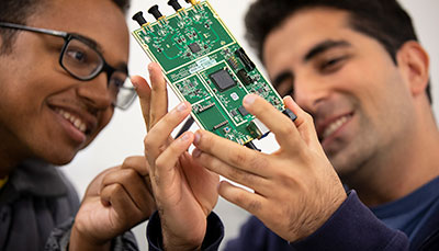 Two students holding up a circuitboard from a computer.