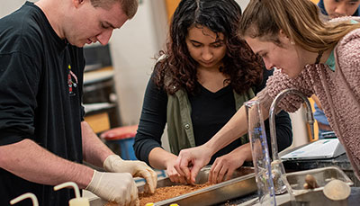 Three students working together sifting through a tray.