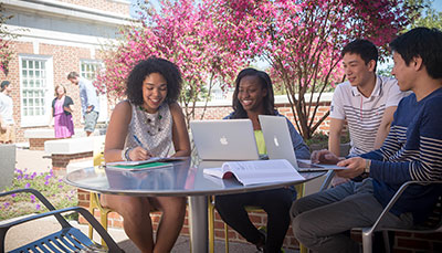 Group of students sitting outside at a table with laptops.