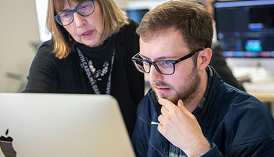 Professor leaning over a student's shoulder looking at a computer screen.