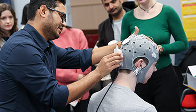 Professor adjusting a device to gather data attached to a silicone cap on a student's head.