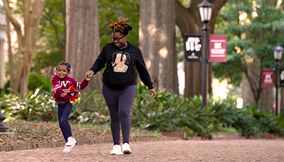 Student holding hands and walking with a young child on the horseshoe. 