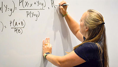 Economics professor writing an equation on a whiteboard. 